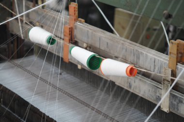 İplikler atölye ortamındaki bir tekstil makinesinden besleniyor.