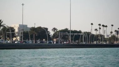 İnsanlar, palmiye ağaçlarıyla dolu, hareketli bir rıhtım boyunca güneşli günün tadını çıkarıyorlar..