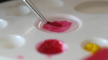 Bir boya fırçası sanat için bir palette pembenin ve kırmızının tonlarını ustalıkla karıştırır.