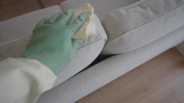 Bir insan rahat bir yerde açık renkli bir kanepeyi kumaşla siler..