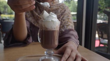 Birisi kafede bir fincan sıcak çikolataya krema karıştırıyor..