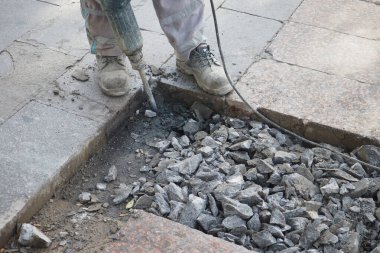 Bir inşaat işçisi kaldırımda eski kaldırımı kaldırmak için kaya matkabı kullanıyor..