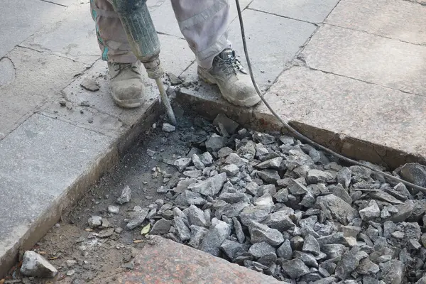 Bir inşaat işçisi kaldırımda eski kaldırımı kaldırmak için kaya matkabı kullanıyor..