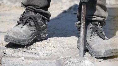 Bir inşaat işçisi şehir merkezinde bir aletle kaldırımı yıkıyor..