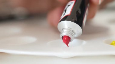 Bir sanatçı canlı kırmızı boyayla paleti renklendirmeye hazırlanır..