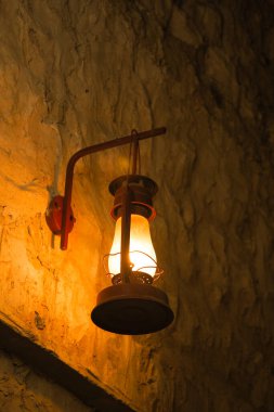 Bir fenerden gelen sıcak bir parıltı dokulu bir taş duvarı vurgular..