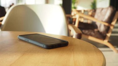 Samimi bir kafe atmosferindeki ahşap bir masanın üzerinde bir akıllı telefon duruyor..