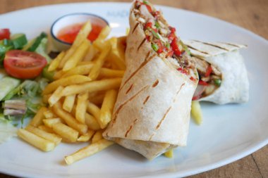 Et ve sebzeli burrito, patates kızartması ve salata ile servis edilir..