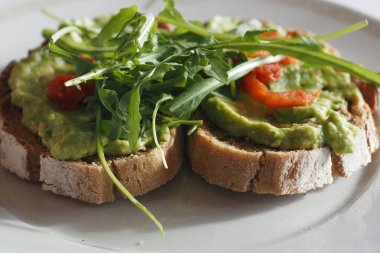 Yeşiller ve kırmızı malzemelerle süslenmiş taze yapılmış avokado tostu..