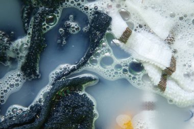 Köpüklerle dolu sabunlu suya batırılmış koyu ve açık renkli giysiler..