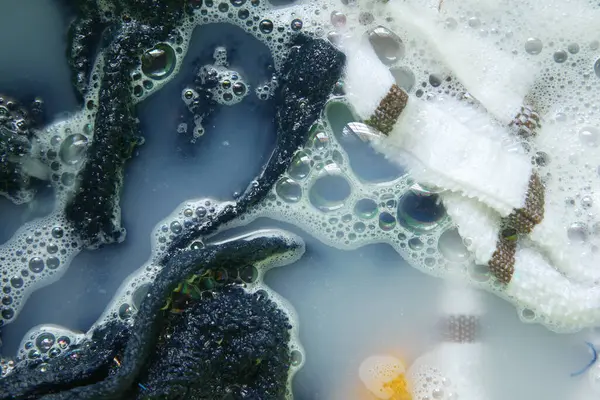 Köpüklerle dolu sabunlu suya batırılmış koyu ve açık renkli giysiler..