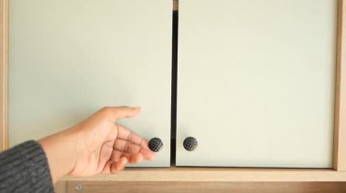Bir el, minimalist tasarım özelliklerine sahip çağdaş bir dolabı açar.