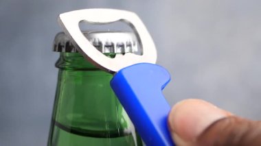 Cam bir içecek şişesinin kapağını açmak için şişe açacağı kullanıyor..