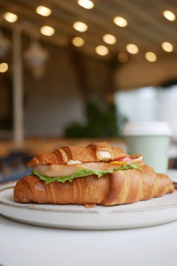 Lezzetli kruvasan sandviçi, taze malzemeler ve kafede kahve..