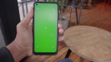 Bir kişi sıcak ve davetkar bir kafe içinde akıllı telefon sergiliyor..