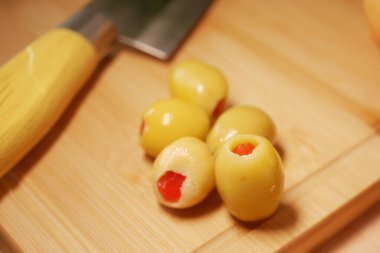 Bıçakla kesme tahtasına yerleştirilmiş kırmızı dolgulu yeşil zeytinler..