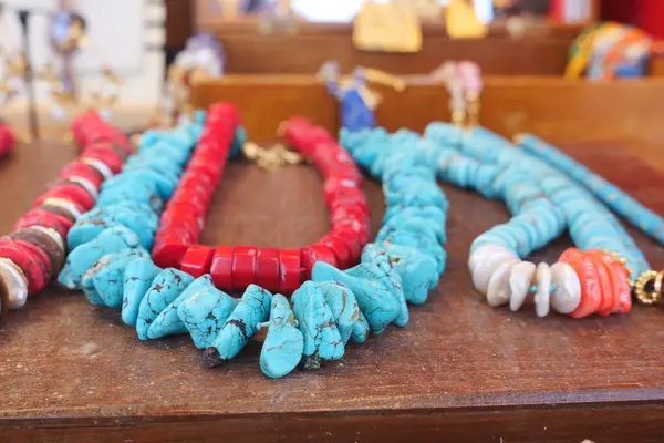 Canlı turkuaz ve ahşap bir masada dizilmiş kırmızı kolyeler..
