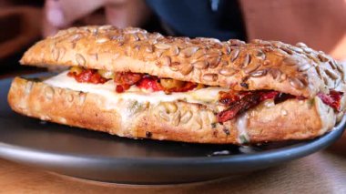 Öğle yemeğinde leziz malzemelerle dolu doyurucu bir sandviçin tadını çıkarıyorum..