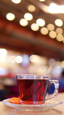 Sıcak çayla dolu berrak bir bardak, yanında portakalla birlikte bir fincan üzerinde oturur..