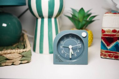 Dekoratif alarm saati renkli ev dekorasyonu öğelerinin yanındaki rafta duruyor.