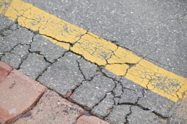 Yıpranmış ve çatlamış bir asfalt yüzeyi bir şehirde solmuş sarı bir çizgi gösteriyor..