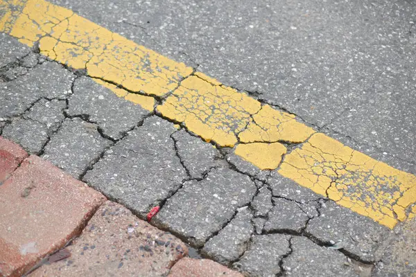 Yıpranmış ve çatlamış bir asfalt yüzeyi bir şehirde solmuş sarı bir çizgi gösteriyor..