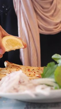 Bir el, tabağında otlar olan sıcak ekmeğin üzerine limon sıkıyor..