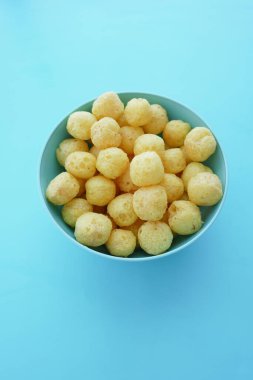 Bir deniz mavisi kasesi mavi bir yüzeye karşı küçük, yuvarlak, altın atıştırmalıklarla doludur..