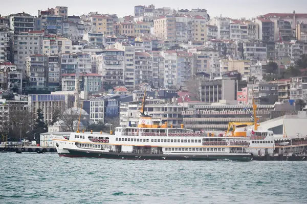 Arka planda şehir binaları olan hareketli rıhtımlara bir feribot geliyor..