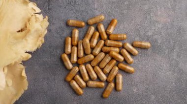 Çeşitli bitkisel kapsüller bir masada kurutulmuş mantarların yanında sergilenir..