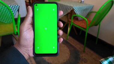 Kişi rahat bir kafe ortamında akıllı telefon görüntüsü sergiler.