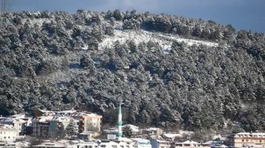 Kar yamacı kaplıyor, köyü ve uzun minaresini çerçeveliyor..