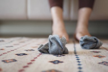 Gri çoraplar rahat ayakların yanındaki desenli bir halıya atılır..