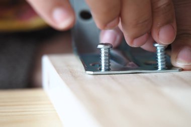 Bir insan tahta bir tahtaya vidayla metal parantez güvence altına alıyor..