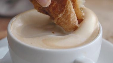 Sıcak bir kafede köpüklü kahveye batırılmış kruvasan..