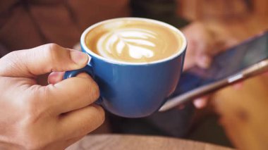 Kapalı mekanda akıllı telefon kullanan biri mavi bardaktan kahve yudumlar..