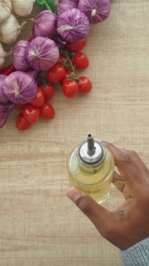 Bir el, ahşap bir masada renkli sebzelerin üzerinde yağ tutar..