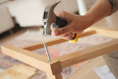 Bir insan çekiç kullanarak tahta bir bacağa vida takıyor..