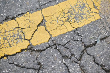 Yol yüzeyinde yağmurdan sonra solmuş sarı şerit boyunca çatlaklar görülüyor..