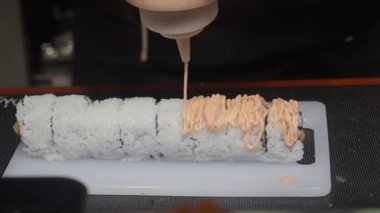 Yetenekli bir şefin lezzetli soslu suşi rulosu yapmasını izleyin..