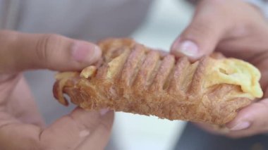 Bir insan taze pişmiş hamur işi tutar, altın katmanlarının ve dokusunun tadını çıkarır..