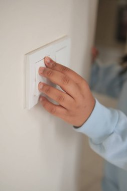 Küçük bir çocuk evindeki bir duvardaki lamba düğmesine uzanıyor..