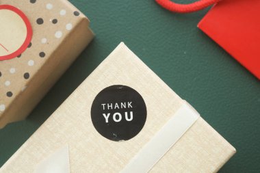 Güzel paketlenmiş bir hediye kutusu yeşil bir masada üzerinde bir teşekkür etiketi ile oturuyor..