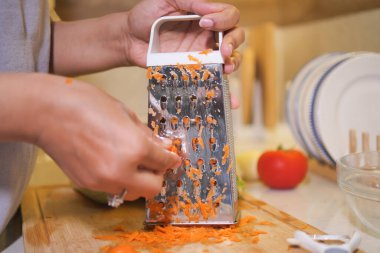 İyi aydınlatılmış bir mutfakta taze salata için el rendeleyici havuç..