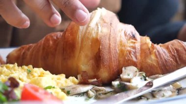 Bir insan çırpılmış yumurta ve sebzenin yanında kruvasanın tadını çıkarıyor..