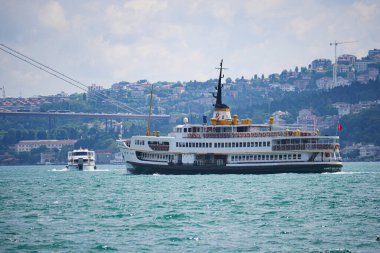 İstanbul 'da, tepeler ve binalarla çevrili bir feribot denize açılıyor..