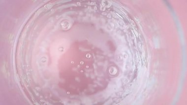 Kabarcıklar oluşur ve berrak bir sıvıyla pembe bir zemine doğru yükselir..