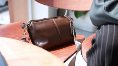 Modern bir kafe ortamında ahşap bir sandalyeye yerleştirilmiş sofistike bir el çantası..