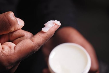 Yumuşak ışıkta konteynırdan krem süren bir elin yakın çekimi.