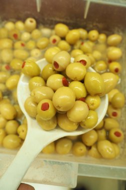 Yeşil zeytinlerle dolu bir kepçe. Kırmızı pimento sergileniyor..